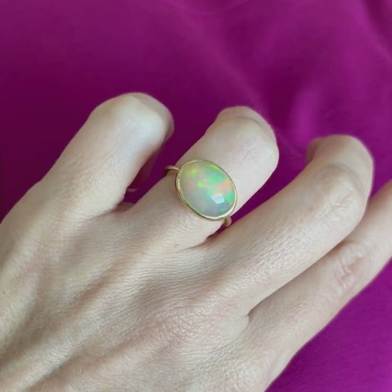 A person wearing a gold cabochon opal ring in a bezel setting.